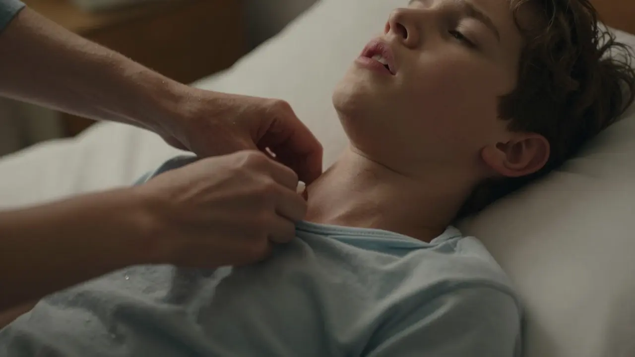 Matka uvolňuje těsný krk dítěte, které leží na posteli s příznaky obtížného dýchání.